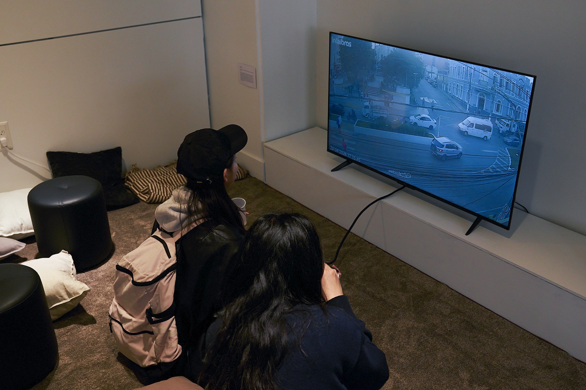 Two people sitting on the floor watching a TV showing a street scene