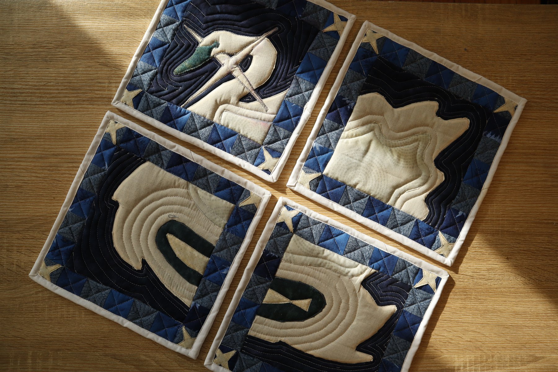 Four quilted swan potholders laid flat